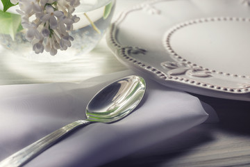 Plate and dessert spoon on white wooden table with white flower in vase.