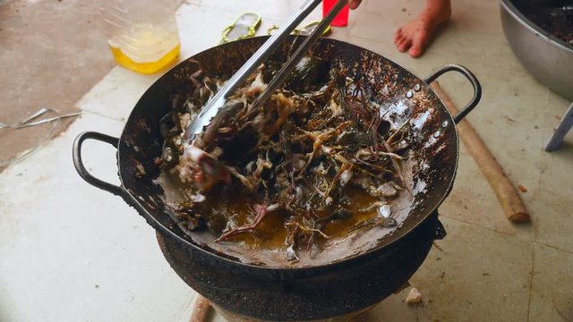  Woman using metal tongs to stir deep-frying frogs in a wok over a household stove ( close up 