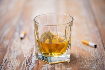 alcohol addiction and alcoholism concept - close up of glass of whiskey and cigarette butts on table