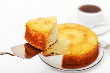 Homemade Pineapple Upside Down Pie with a piece cut off and cup of tea on white wooden table. Shallow focus.