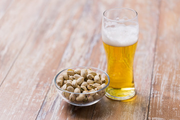 food and drinks concept - glass of draught beer and pistachio nuts on table