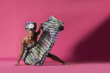 Beautiful African Black girl wearing traditional colorful African outfit does a dramatic dance move against a colorful pink background