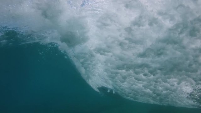 SLOW MOTION, UNDERWATER: Powerful deep blue barrel wave pushes unrecognizable surfer to shore. Unknown extreme surfer dares to ride a rushing crystal clear tube wave. Breathtaking force of nature.