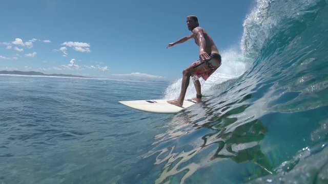 SLOW MOTION, UNDERWATER, CLOSE UP: Athletic surfboarder rides a big blue barrel wave towards the shore in spectacular Fiji. Cheerful surfer carving an epic Cloudbreak wave on a perfect summer day.