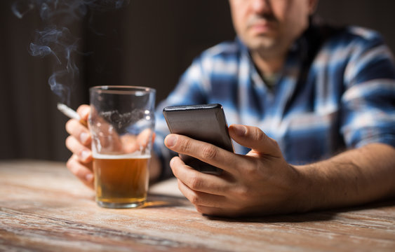 Alcoholism, Alcohol Addiction And People Concept - Male Alcoholic With Smartphone Drinking Beer And Smoking Cigarette At Night