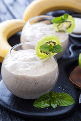 fresh banana smoothie with apple, kiwi and mint on a black wooden table.