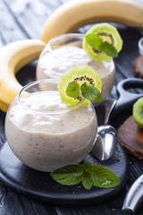 fresh banana smoothie with apple, kiwi and mint on a black wooden table.