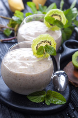fresh banana smoothie with apple, kiwi and mint on a black wooden table.
