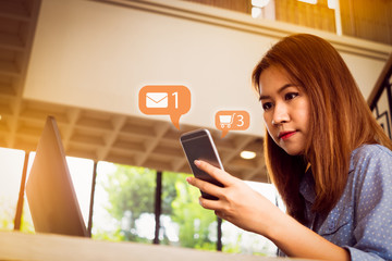 Social media or social network notification icons with female freelancer using mobile phone and laptop on the wooden table in vintage cafe coffee shop, Big data and digital networking concept