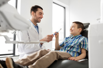 medicine, dentistry and healthcare concept - male dentist giving toothbrush to kid patient at dental clinic