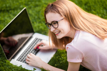 Girl in glasses with laptop lying on the lawn