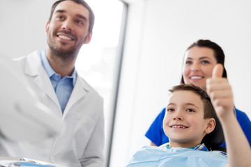 Obraz premium medicine, dentistry and healthcare concept - dentists and happy kid patient at dental clinic showing thumbs up
