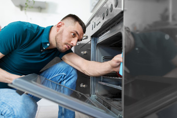 household and people concept - man wiping table with cloth cleaning inside oven at home kitchen