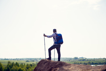 Photo of back of tourist man with backpack and walking sticks on hill