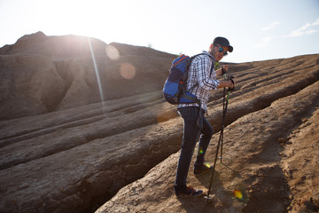 Photo of tourist man with walking sticks in mountainous area against sun