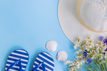 Summer hat, flowers and flip flops on a blue background
