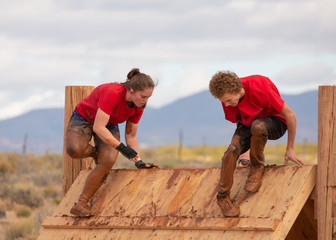 Teenage boy and girl climbing over an obstacle in a mud run obstacle course