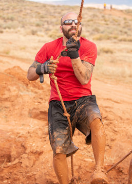 A Man In Sunglasses And A Red Shirt Climbing Up Out Of A Mud Pit During A Mud Run Obstacle Course