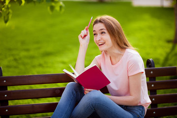 Obraz premium Girl is thinking what to write in a notebook, sitting in the Park