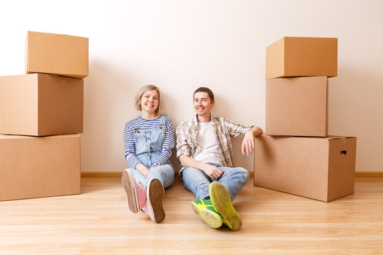 Photo of young married couple sitting on floor among cardboard boxes