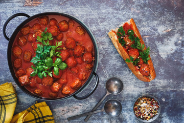 Meatballs with tomato sauce in pot and delightful sub sandwich beside. Top view, blank space