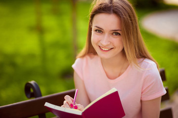 girl writes in a notebook, sitting on a bench in the Park