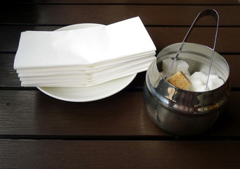 A stack of paper napkins and a sugar bowl on a wooden table