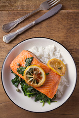 Salmon fillet with rice and spinach garnish. Fish steak. Lemon salmon on white plate on wooden background. overhead, vertical