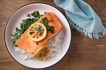 Salmon fillet with rice and spinach garnish. Fish steak. Lemon salmon on white plate on wooden background. overhead, horizontal