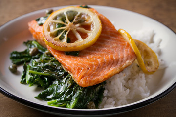 Salmon fillet with rice and spinach garnish. Fish steak. Lemon salmon on white plate on wooden background. horizontal