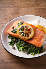 Salmon fillet with rice and spinach garnish. Fish steak. Lemon salmon on white plate on wooden background. vertical