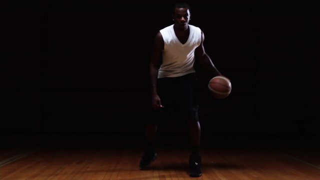 A basketball player dribbles down the court out of the shadows
