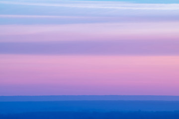 Obraz premium Varicolored striped surreal sky with shades of blue, cyan, pink, purple, magenta colors with cobalt land. Horizontal lines of smooth clouds. Atmospheric background image of tender sky.