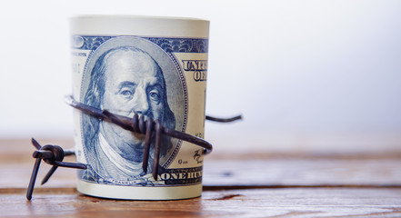 US Dollar money wrapped in barbed wire as symbol of economic warfare, sanctions and embargo busting