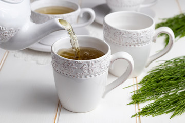 Pouring horsetail tea into a cup on a table