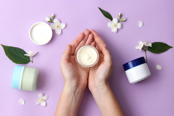cream and female hands on a pastel background. a composition of flowers, a care cream and hands. minimalism. anti-aging cream. skin care. flatly