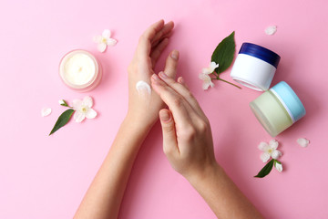 beautiful female hands and cosmetic cream and flowers on a colored background. To smear arms or hand with a cream, an elastic skin.