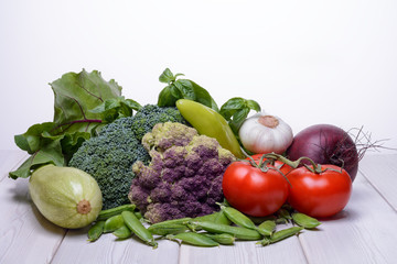 Various fresh vegetables are on a wooden table and on a white background