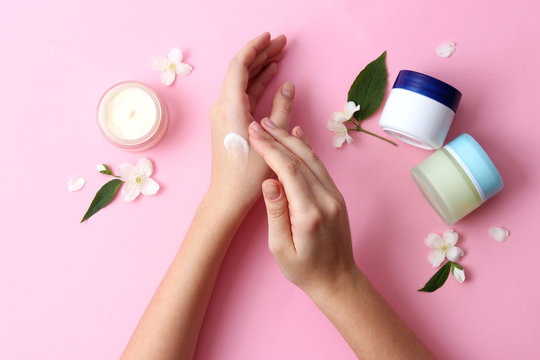 Beautiful Female Hands And Cosmetic Cream And Flowers On A Colored Background. To Smear Arms Or Hand With A Cream, An Elastic Skin.