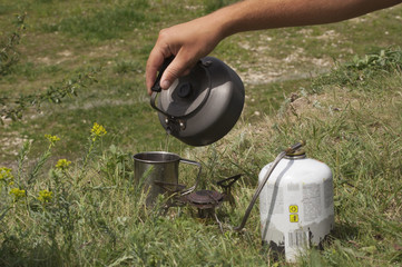 A tourist pours tea from a teapot in a metal cup. To make tea on a gas burner
