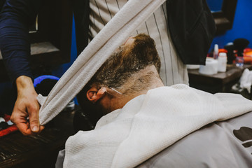 The barber shears the beard and mustache of a man with a hipster.