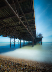 Brighton Pier with a view of the underneath of the pier and the waves with the beach in the foreground 