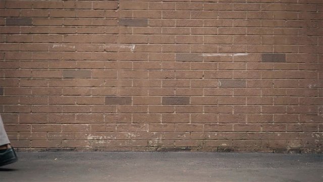 Legs of an unrecognizable man walking past a brick wall on a cold autumn day. Tracking slow motion medium shot