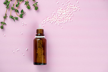 Flat lay of brown glass bottle with plenty of white homeopathic pills on pink surface. Homeopathic lactose sugar balls in glass bottles,medicine. Bottle with white sugar pills