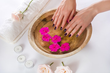 Obraz na płótnie Canvas Female hands with manicured fashion nails with purple varnish in a wooden bowl with water and purple flower. Spa beauty treatment concept. Close up, selective focus