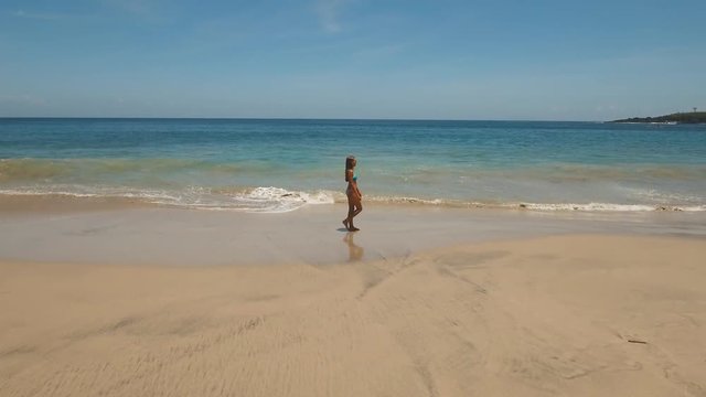 Young girl in a swimsuit walking on the beach. Aerial view ofBeautiful girl on sandy beach walking along the coast among the waves. Travel concept, Aerial footage, 4K video.