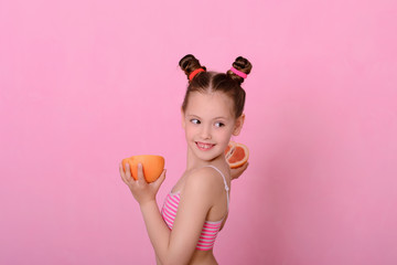 Obraz na płótnie Canvas Caucasian beautiful little girl with grapefruit on a pink background