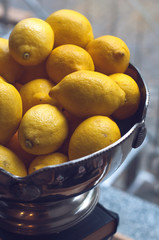 Fresh lemons on vintage metal bowl on a light board. Selective focus. Free space for text. Side view