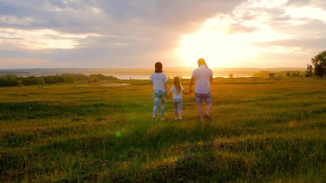 A family with children is walking along the green meadow towards the sunset. Run, raising baby up in the air, hugs, love, playing. We are happy family.