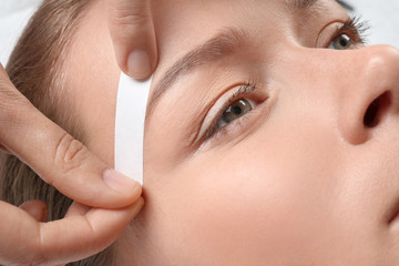 Young woman having eyebrow correction procedure in beauty salon, closeup